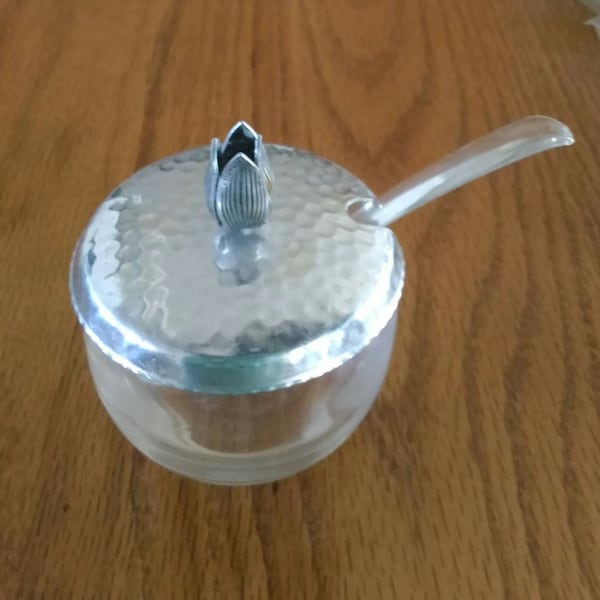 Glass condiment jar, a small plastic serving spoon, and with a notched hammered metal lid with a tulip finial.  Dish 871