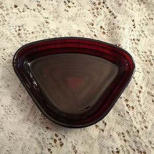 May include: A dark red glass triangular dish with a smooth, shiny surface.