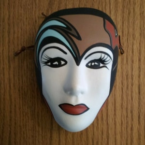 A ceramic carnival mask with mesmerizing sold eyes decorated with brown, black, burnt orange, and light blue.  Misc 1066