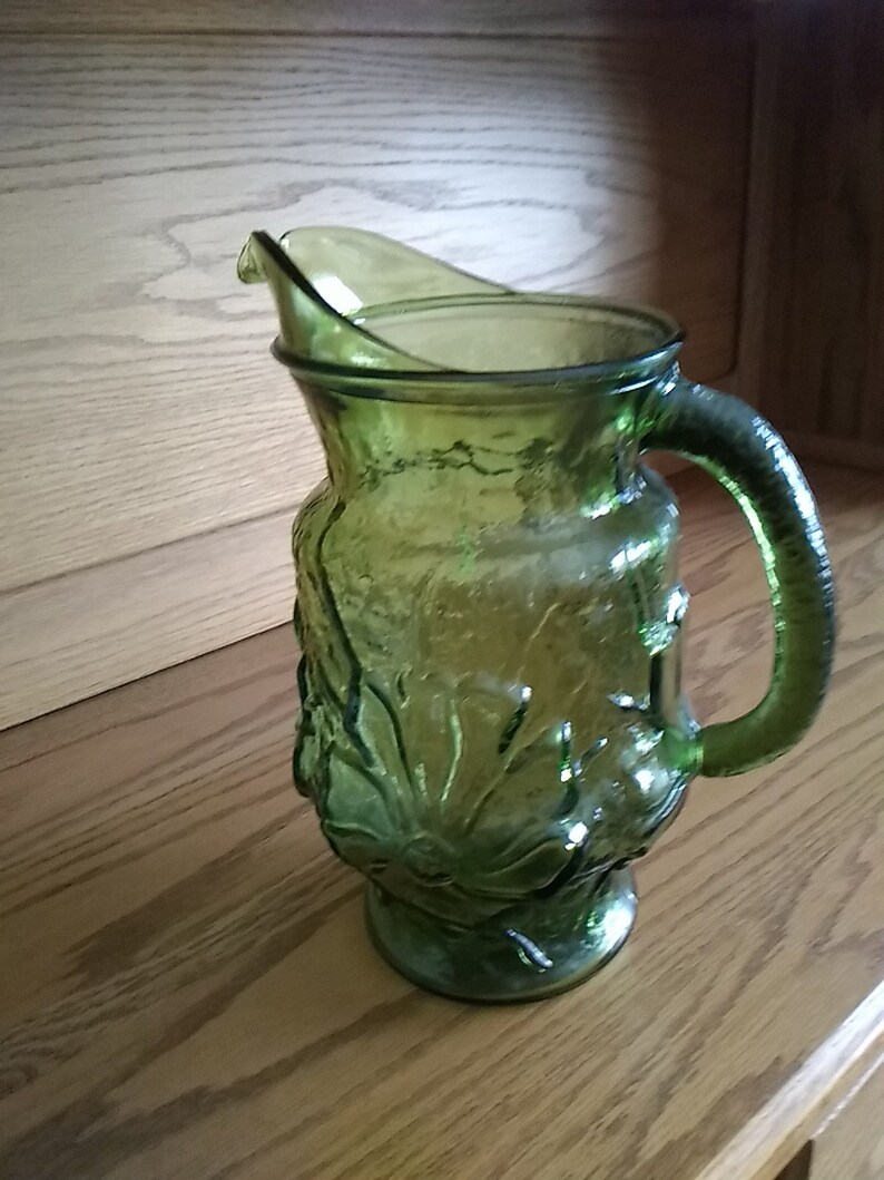 A large green glass pitcher with an embossed floral ...