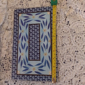 May include: A blue and white glass cutting board with a decorative border of blue leaves and yellow flowers. The board measures 9 inches by 13 inches.