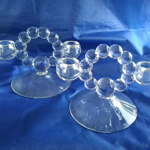 May include: Two clear glass candle holders with a beaded design. Each holder has three candle cups and a circular base.