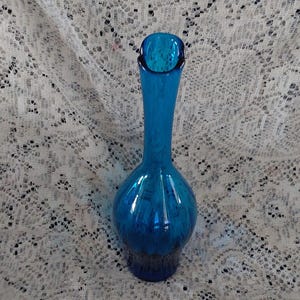 May include: A tall, turquoise glass vase with a slender neck and a bulbous base. The vase has a glossy finish and a dark blue rim. The vase is approximately 10 inches tall.