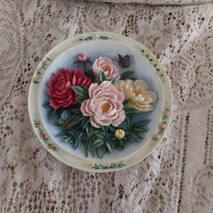 May include: A decorative ceramic plate with a raised design of pink, white, and red peonies with green leaves and two butterflies.