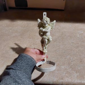 May include: White metal cherub figurine holding a bunch of grapes. The cherub is attached to a white metal ring.