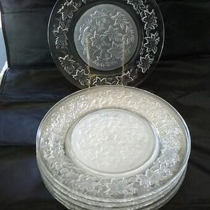 May include: A set of six clear glass dinner plates with a frosted floral design. The plates are stacked on top of each other.