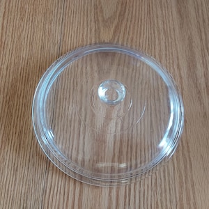 May include: A clear glass lid for a pot or casserole dish. The lid has a small knob in the center.
