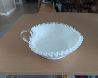 May include: White milk glass bowl with a scalloped edge and a clear glass handle. The bowl is on a wooden surface.