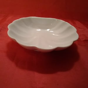 May include: A white ceramic bowl with a scalloped edge. The bowl is empty and has a smooth, glossy finish.