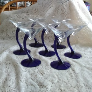 May include: Set of six cobalt blue stemmed martini glasses. The glasses are clear with a cobalt blue stem and base.
