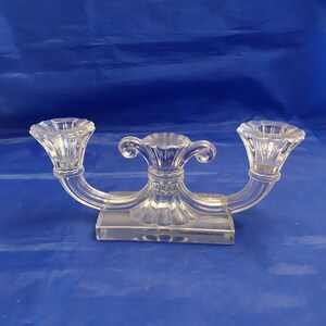 May include: A clear glass three-arm candelabra with a rectangular base and ornate details.