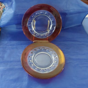 May include: Two vintage glass plates with a red iridescent finish and a clear, raised, circular pattern around the edge. The plates are stacked on top of each other.