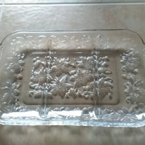 May include: Clear glass serving tray with four divided sections and a floral design. The tray has handles on the sides.