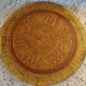 May include: A large, amber-colored glass serving plate with a raised, embossed design of flowers and leaves. The plate has a scalloped edge.