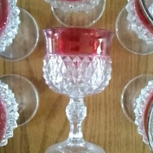 May include: Set of six clear glass wine glasses with a diamond pattern and a red rim. The glasses have a stemmed base.