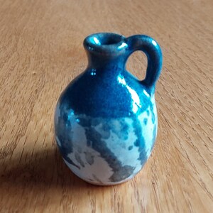 May include: A small, blue and white ceramic pitcher with a rounded body and a handle. The pitcher has a speckled glaze.