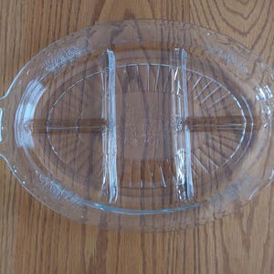 May include: Clear glass oval serving dish with three divided sections. The dish has two handles and a textured design on the rim and interior. Ideal for serving appetizers or snacks.