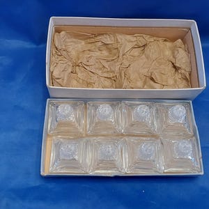 May include: A set of eight clear glass salt and pepper shakers in a white box with brown paper packing. The shakers are square with a small round top.