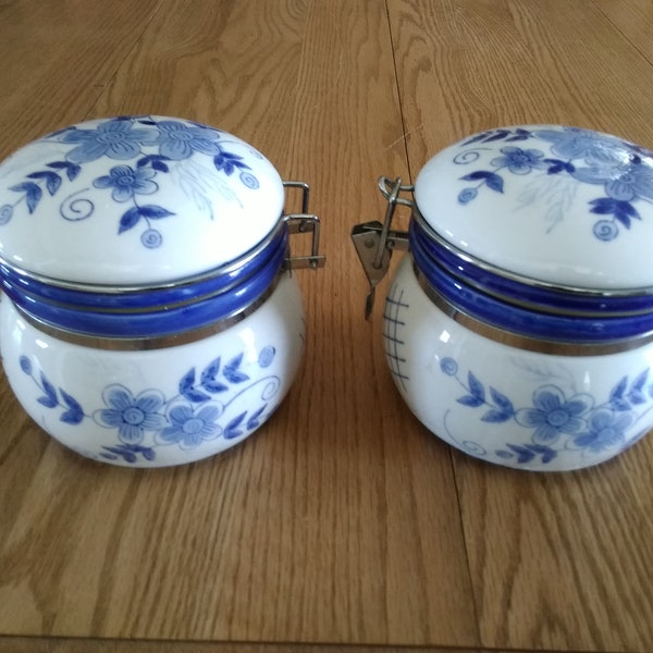 Two white 5.25" tall ceramic canisters with bright blue flowers and design with a rubber seal and bail wire clamp latch.  Canister 7