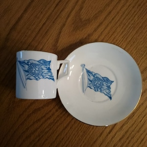 White souvenir demitasse cup and saucer a blue United Nations flag with gold trim made by Kent China company in England.  CS 256