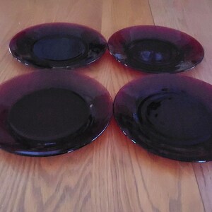 May include: A set of four round plates made of deep purple translucent glass. Each plate features a smooth, reflective surface with a slightly darker center and a lighter, vibrant purple rim, arranged in a two-by-two grid formation.