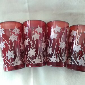May include: Set of four red glass tumblers with a white floral design. The glasses are clear and have a vintage look.