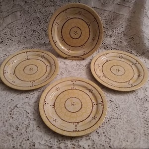 May include: Set of four yellow ceramic dinner plates with a brown floral design. The plates have a raised rim and a slightly scalloped edge.