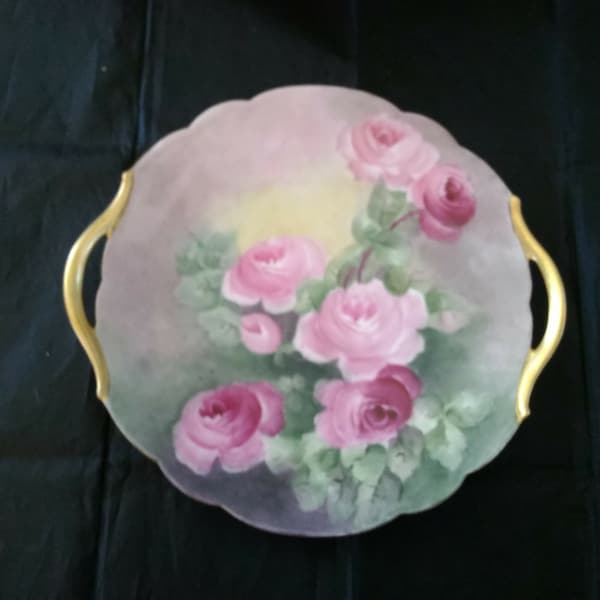 An antique T&V Limoges France plate, hand painted and signed by Stewart, is a pink rose design with gold handles.  Plate 566