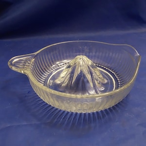 May include: A clear glass citrus juicer with a ridged exterior and a central cone for squeezing fruit. The juicer has a handle on one side.