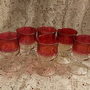 May include: Six clear glass goblets with a ruby red colored base. The goblets have a clear, textured design.