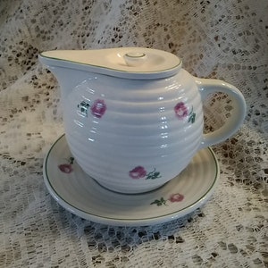 May include: White ceramic creamer with a green rim and pink rose pattern. The creamer has a lid and a matching saucer.