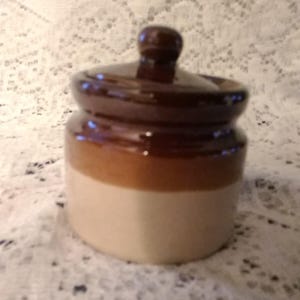 Attributed to Armbee, is a small stoneware jam jar or spice pot in a tri-colored beige and browns with a match lid.  SW 211