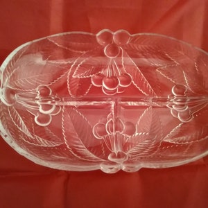May include: A clear glass serving dish with a divided center. The dish is decorated with a raised design of leaves and cherries.