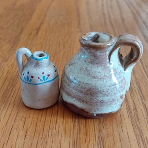 May include: Two small ceramic jugs, one with a brown and white swirl pattern and the other with a white base and blue and red painted details.