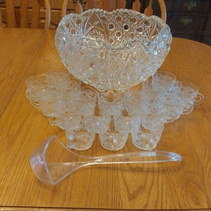 May include: A clear glass punch bowl with a cut glass design and a matching set of 12 cups and a ladle.