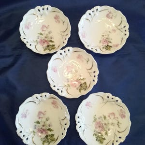 May include: Set of five white porcelain bowls with delicate floral designs in pink and green. The bowls have a scalloped edge and openwork design around the rim.