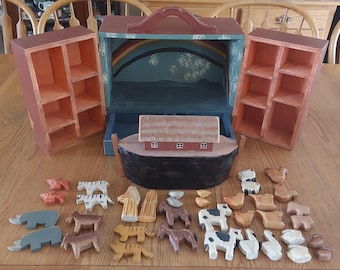 May include: A wooden toy Noah's Ark playset with a blue and green painted interior. The ark has a brown roof and a black hull. The set includes a variety of wooden animal figurines, including a pair of elephants, a pair of giraffes, a pair of lions, a pair of zebras, a pair of cows, a pair of sheep, a pair of pigs, a pair of horses, a pair of donkeys, a pair of goats, a pair of chickens, a pair of ducks, a pair of geese, a pair of turkeys, a pair of rabbits, a pair of squirrels, a pair of mice, a pair of cats, a pair of dogs, a pair of bears, a pair of monkeys, a pair of snakes, a pair of fish, a pair of birds, and a pair of butterflies.