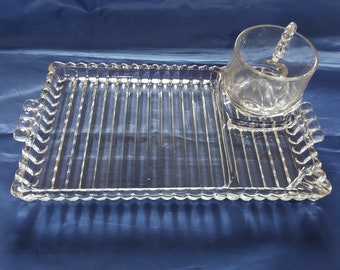May include: A clear glass serving tray with a raised, ribbed design. The tray has a small, separate compartment for a condiment dish or small bowl.