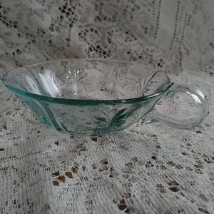 May include: A clear glass bowl with a handle. The bowl has a scalloped edge and a floral design.
