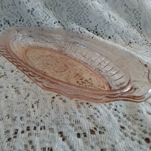 May include: A pink glass oval dish with a scalloped edge and a textured design. The dish is made of clear glass with a pink tint.