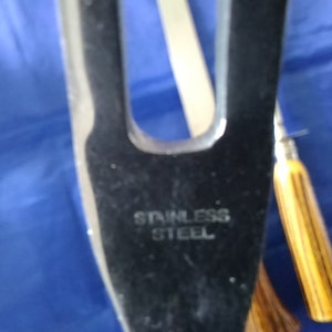 K&ouml;nnte beinhalten: Nahaufnahme einer Edelstahl-Schnitzgabel mit einem Holzgriff. Die Gabel hat zwei Zinken und ist mit "Stainless Steel" gekennzeichnet.