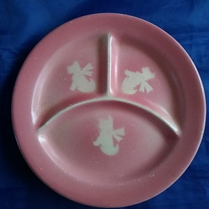 May include: A pink divided plate with three sections. Each section has a white silhouette of a dog with a bow.