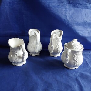 May include: Four white ceramic salt and pepper shakers with intricate floral designs. The shakers are arranged on a blue surface.