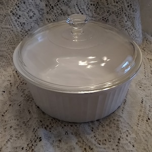 May include: White ceramic baking dish with a glass lid. The dish has a fluted design around the rim.