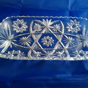 May include: A clear glass serving dish with a starburst pattern. The dish is oval shaped and has a scalloped edge.