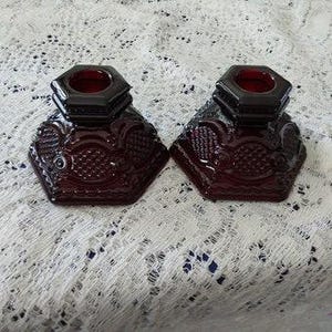 May include: A pair of ruby red glass candle holders with a hexagonal base and a textured design.