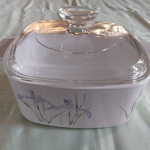 May include: White casserole dish with a clear glass lid and a clear glass handle. The dish has a floral design with blue and purple irises. The dish has two handles on either side.