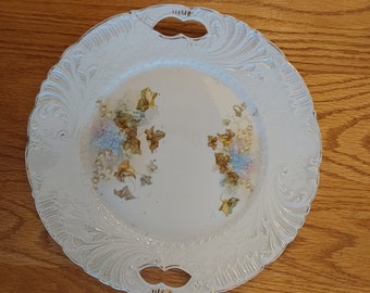 An antique white porcelain serving plate from the early 1900s with cut outs for handles, embossed plate with blue floral design.  Plate 837