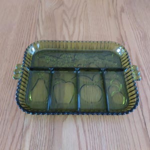 May include: A vintage green glass serving tray with four divided sections and a decorative fruit design. The tray has a rectangular shape with scalloped edges and handles on each side. The fruit designs include pears and apples.