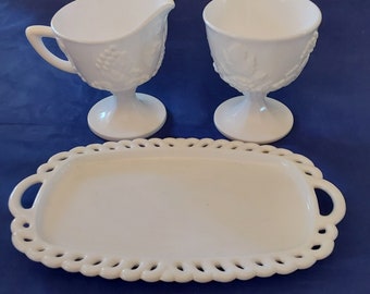 Puede incluir: Un juego de servicio de vidrio de leche blanco con una jarra de crema, un azucarero y una bandeja con un borde de diseño de cuerda.